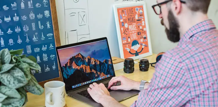 Person working on laptop in a creative workspace, surrounded by plants and photography equipment, illustrating digital marketing strategies for porta potty rental businesses.